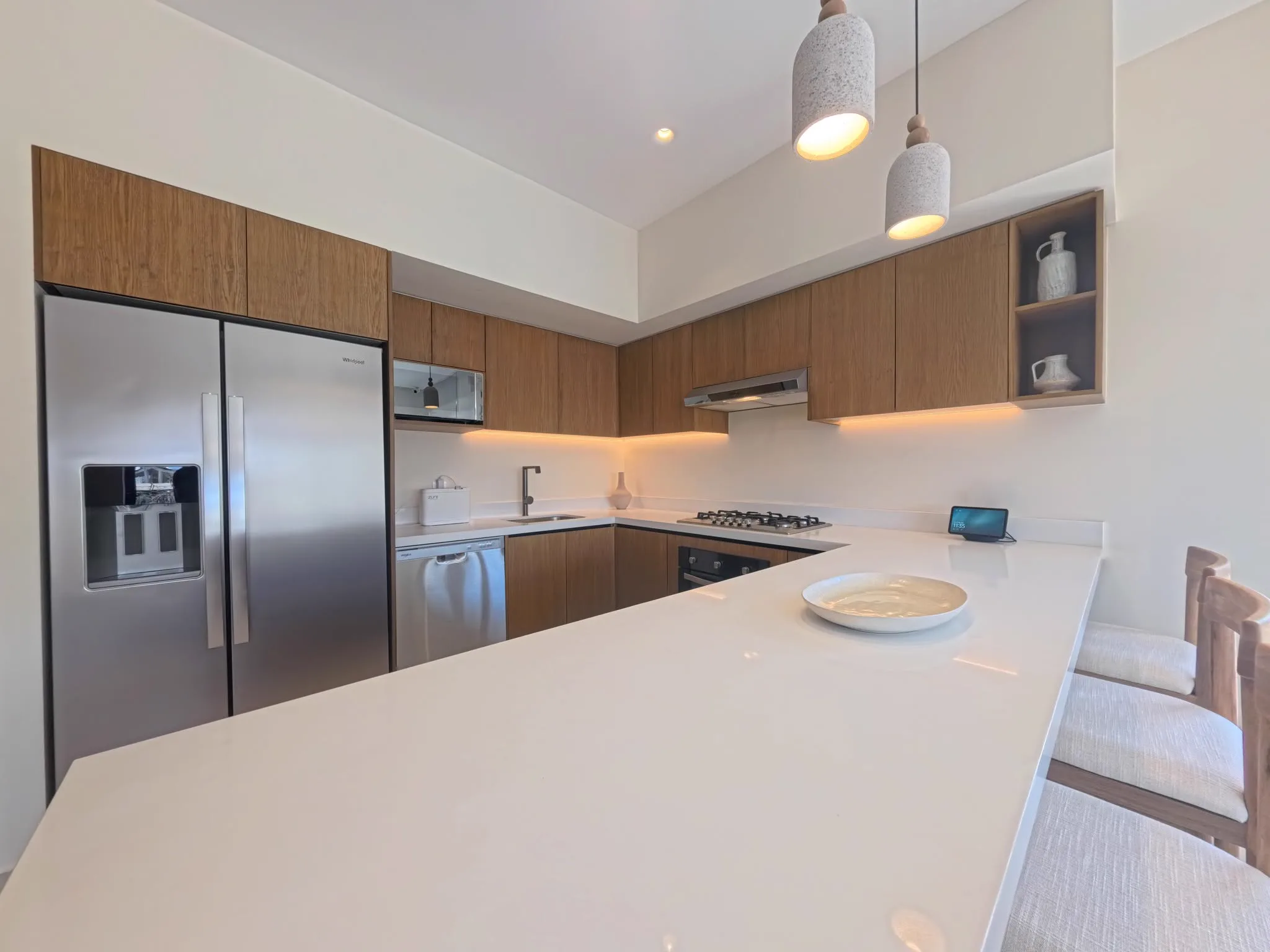 Cocina de Olympia con isla de cuarzo blanco, gabinetes de madera y refrigerador de dos puertas
