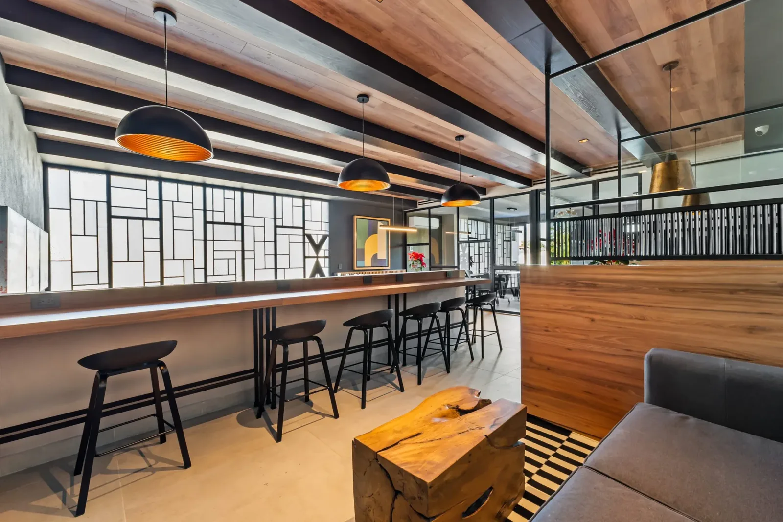 Área de coworking con barra larga de madera, bancos negros y lámparas colgantes