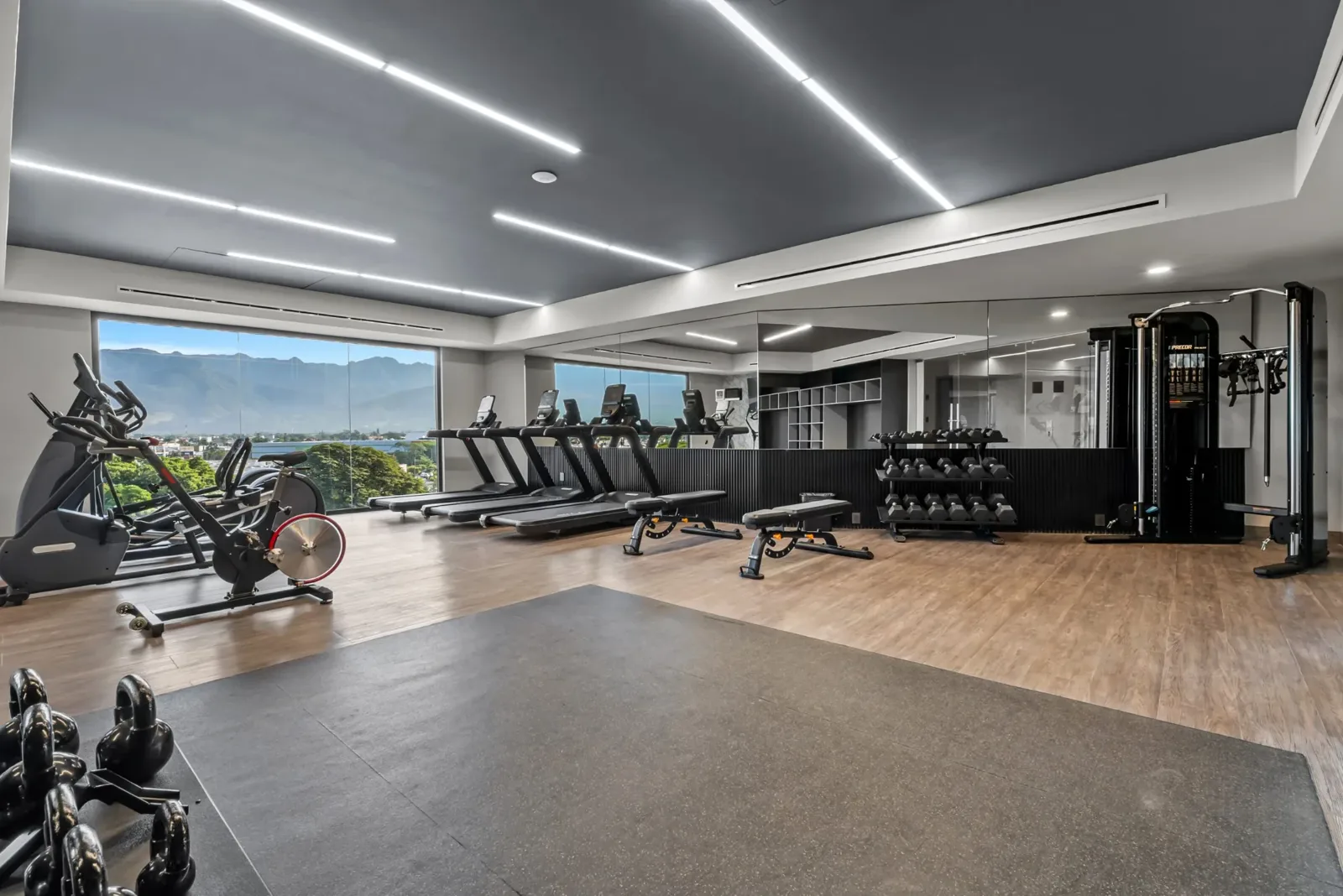 Gimnasio equipado con caminadoras, bicicletas, mancuernas y ventanales con vista a las montañas
