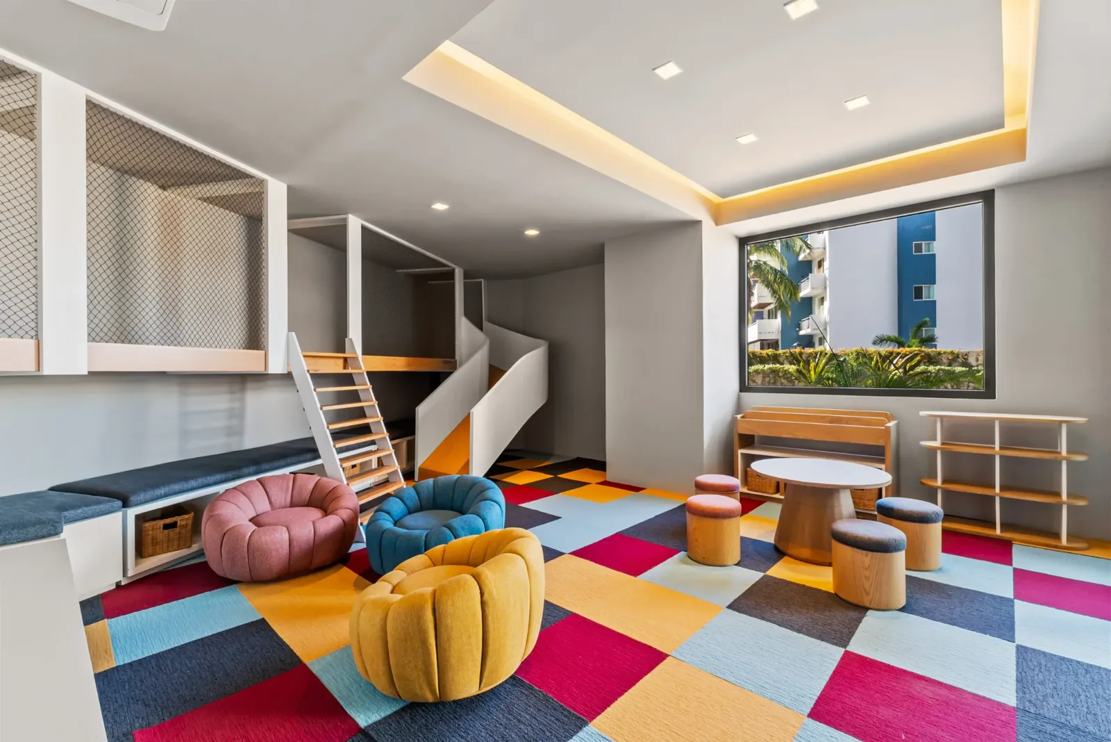 Salón de juegos infantil interior con resbaladilla, escalera, sillones de colores y alfombra geométrica