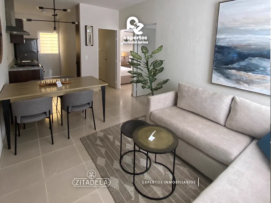 Sala y comedor del departamento muestra de Zitadela con sofá, mesa de centro y cocina al fondo